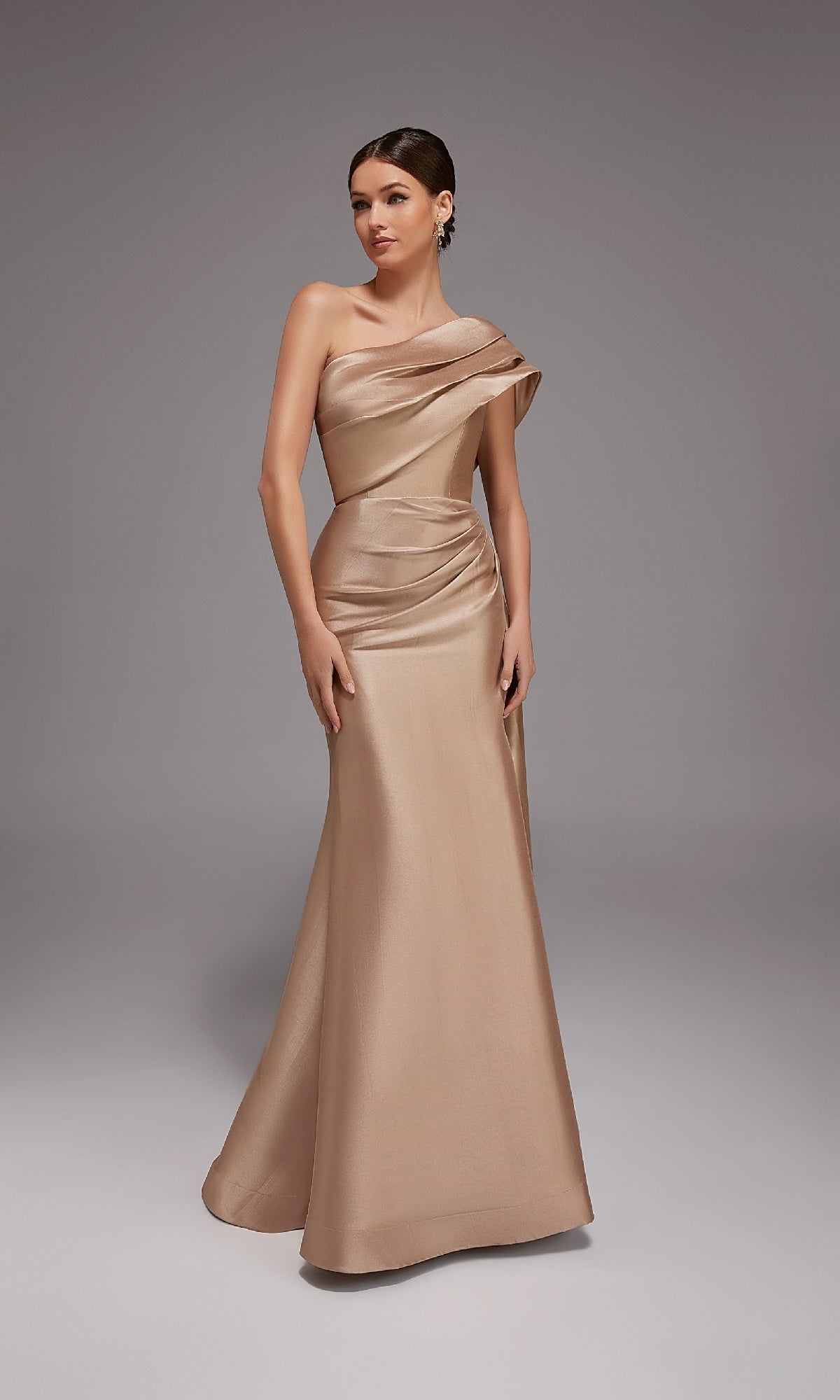 A woman models the Alyce 27838 Long Formal Dress in sand, featuring a floor-length mermaid silhouette, draped detailing, and a one-shoulder evening design against a plain gray background.